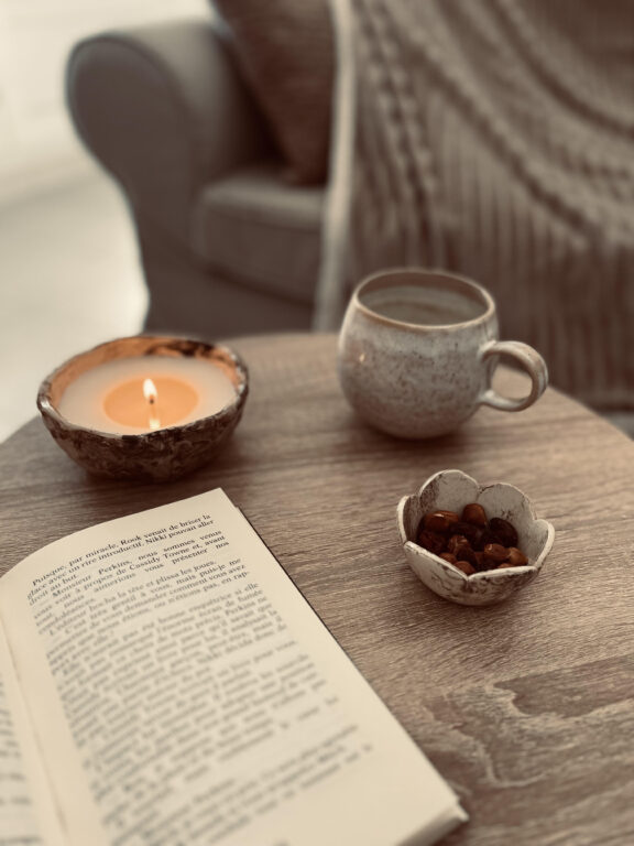 une bougie, un livre ouvert et un mug sur une table basse près d'une canapé