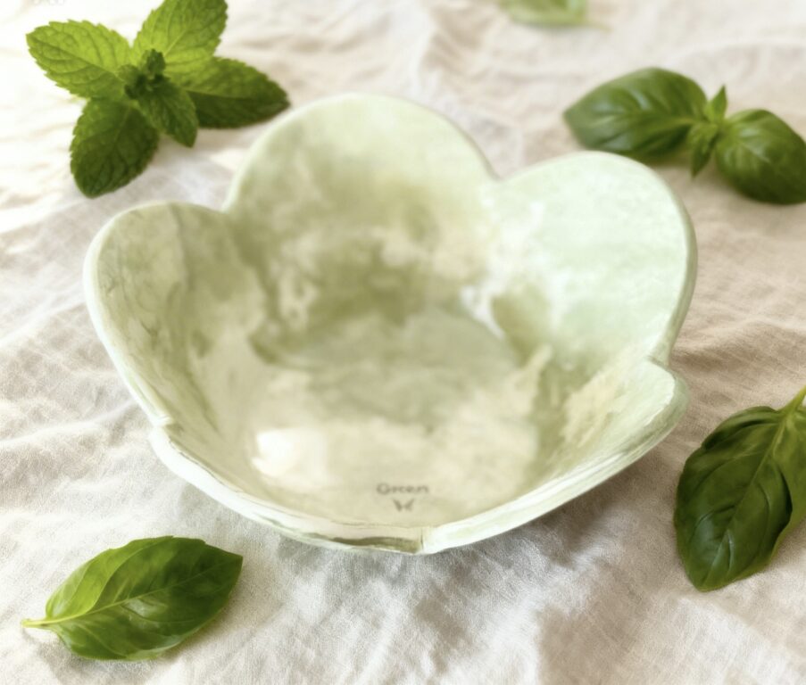 Bol fleur vert & blanc posé sur une nappe en lin et un eparpillement de feuilles de basilic