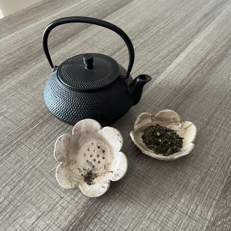 Un infuseur a thé en forme de fleur en terre melee stracciatella avec une théière en fonte noire